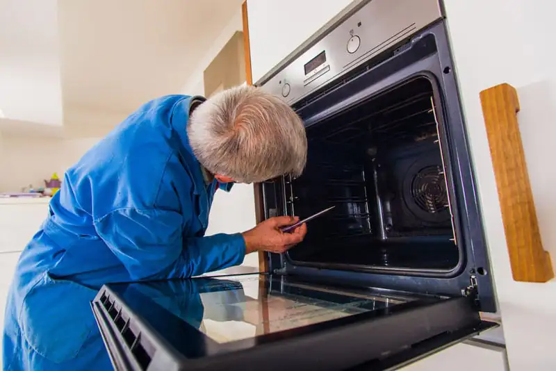 Mature workman fixing oven Mature workman fixing oven